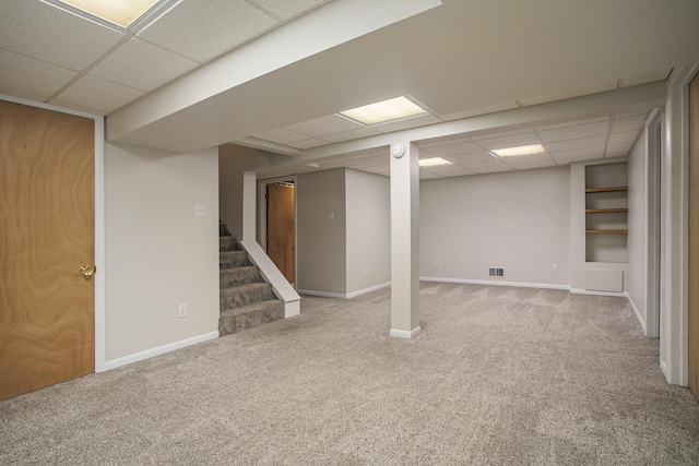 finished basement with carpet floors, baseboards, stairway, and a paneled ceiling