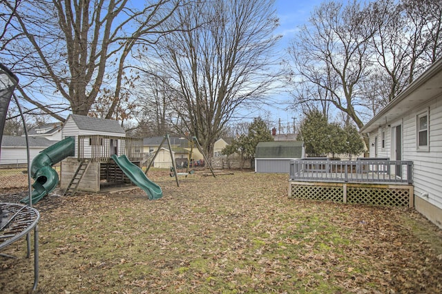 view of yard with fence, a deck, an outdoor structure, a shed, and a playground