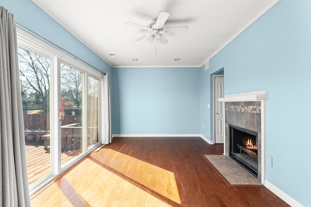 unfurnished living room featuring wood finished floors, a ceiling fan, baseboards, ornamental molding, and a tiled fireplace