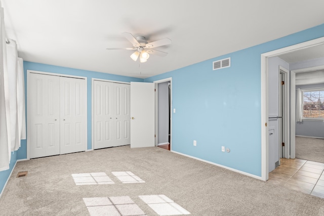 unfurnished bedroom featuring baseboards, carpet flooring, visible vents, and multiple closets