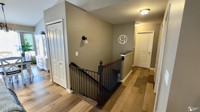 corridor featuring light wood-style floors, a chandelier, baseboards, and an upstairs landing