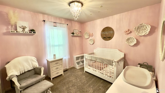 bedroom featuring a nursery area, dark colored carpet, and a notable chandelier