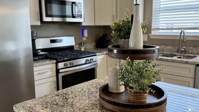 kitchen featuring stainless steel appliances, white cabinetry, a sink, and light stone countertops