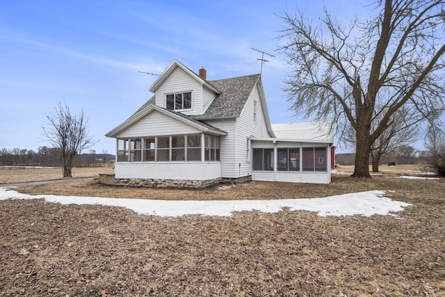 exterior space with roof with shingles, a chimney, and a sunroom