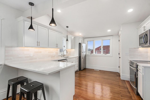 kitchen with hardwood / wood-style flooring, stainless steel appliances, a peninsula, a sink, and a kitchen breakfast bar