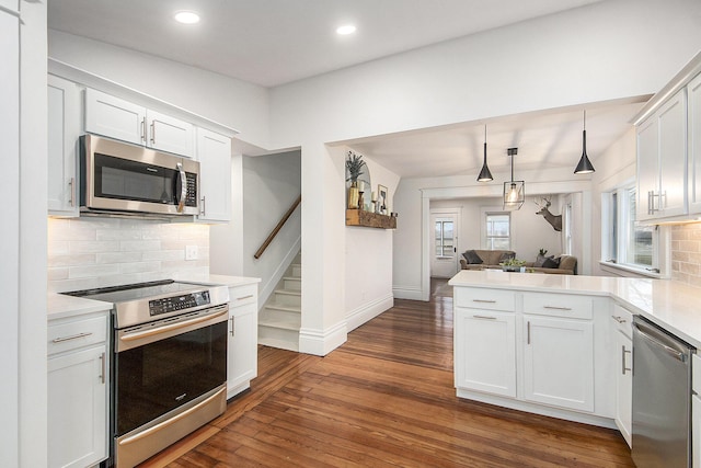 kitchen with stainless steel appliances, a peninsula, open floor plan, light countertops, and dark wood-style floors