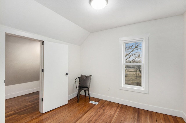 unfurnished room with lofted ceiling, wood-type flooring, visible vents, and baseboards