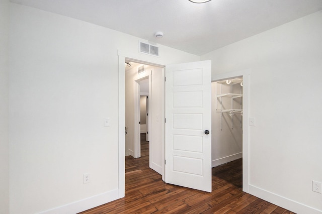 unfurnished bedroom with baseboards, visible vents, dark wood-style floors, a walk in closet, and a closet