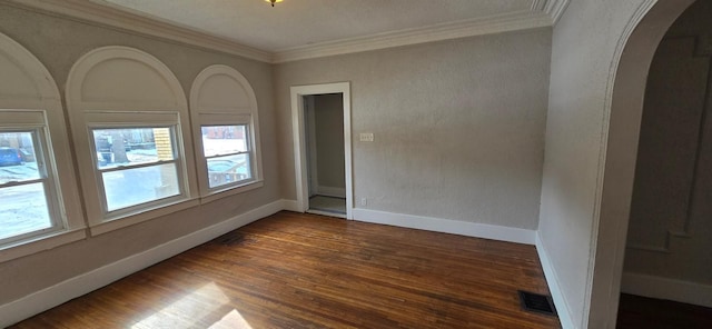 spare room featuring baseboards, visible vents, arched walkways, ornamental molding, and dark wood-type flooring