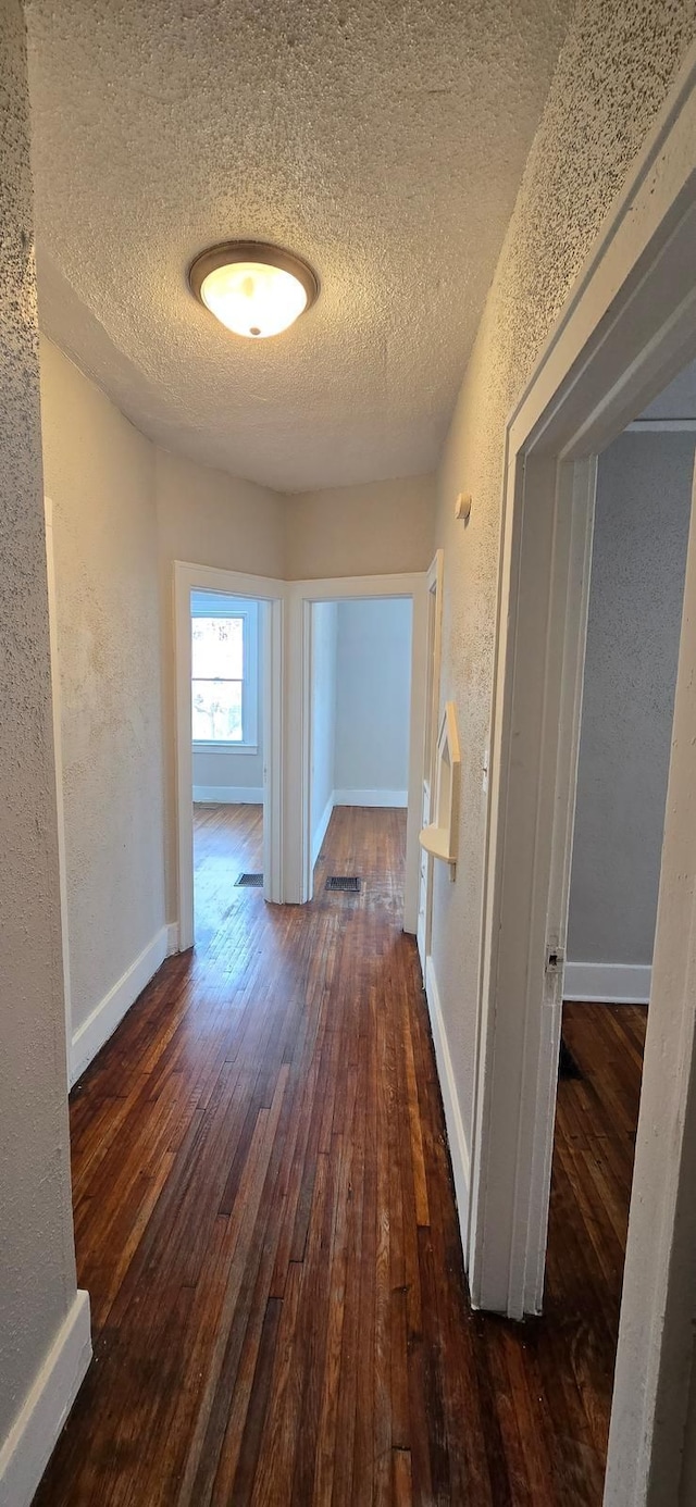 hallway featuring a textured ceiling, a textured wall, hardwood / wood-style floors, and baseboards