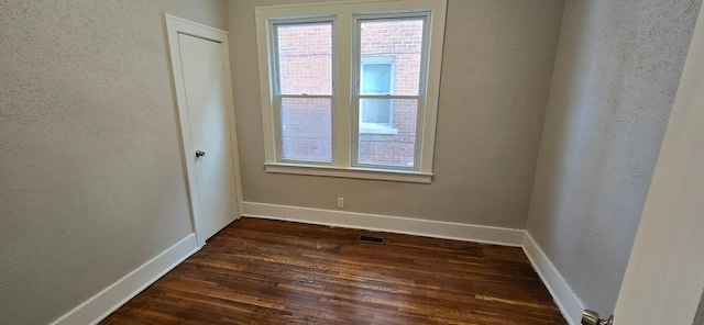 unfurnished room with baseboards, dark wood-type flooring, and a textured wall