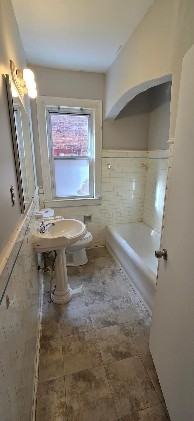 full bathroom featuring a bathtub, a wainscoted wall, tile walls, toilet, and tile patterned flooring