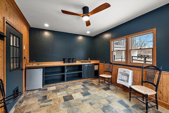 interior space featuring ceiling fan, stone finish floor, wainscoting, and heating unit