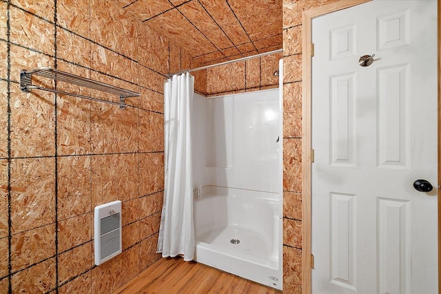 bathroom with heating unit, a shower with shower curtain, and wood finished floors