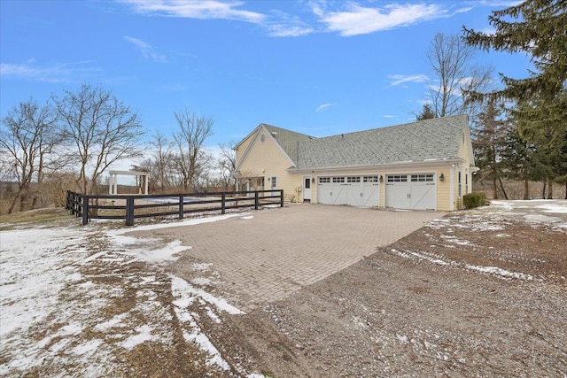 snow covered property with a garage, decorative driveway, and fence