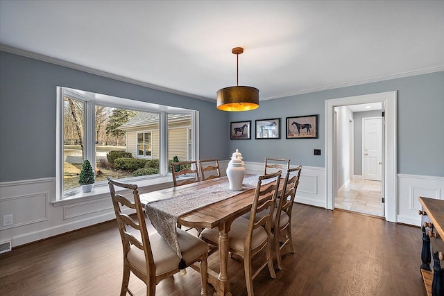 dining space featuring ornamental molding, a decorative wall, a wainscoted wall, and dark wood-style floors