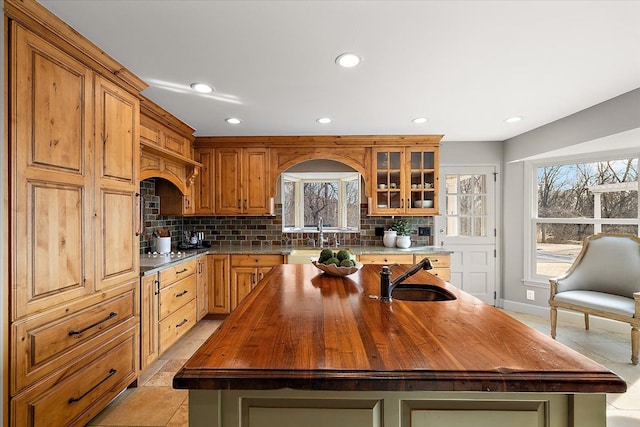 kitchen featuring a sink, tasteful backsplash, butcher block countertops, and an island with sink