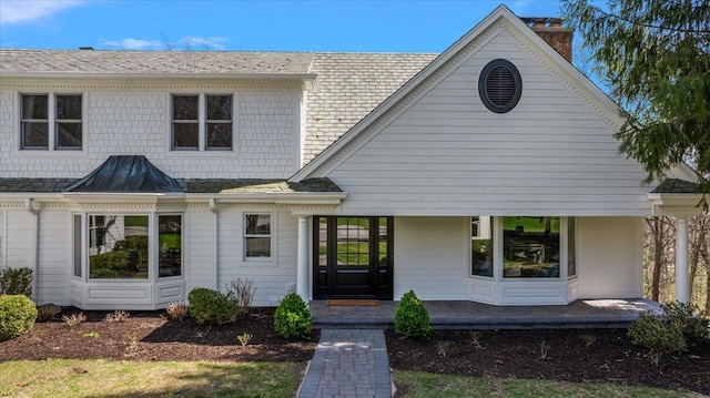 view of front of house with covered porch, a chimney, and a shingled roof