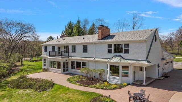 back of house featuring a chimney, decorative driveway, a balcony, a standing seam roof, and a patio