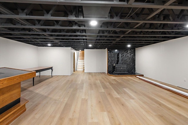 finished basement with stairway, a wood stove, and wood finished floors