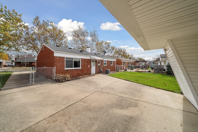 exterior space with a lawn, a chimney, a gate, central air condition unit, and brick siding