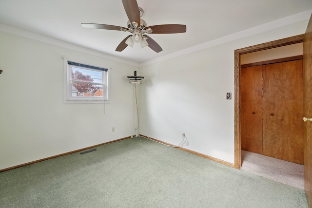 carpeted spare room with ornamental molding, visible vents, ceiling fan, and baseboards