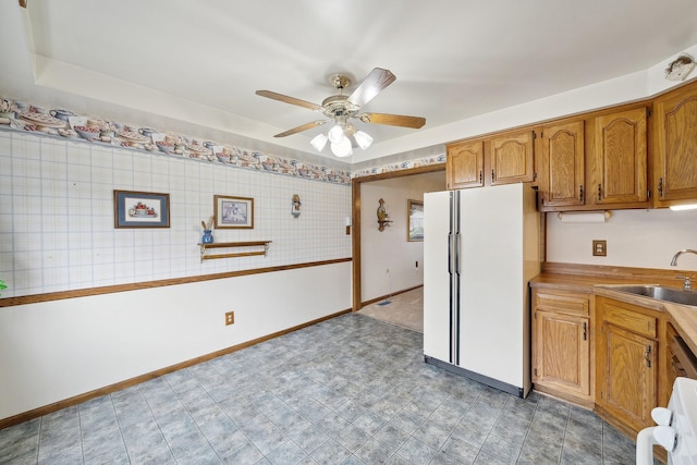 kitchen with light countertops, brown cabinetry, freestanding refrigerator, a sink, and ceiling fan