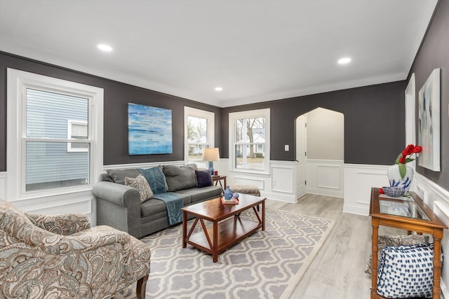 living area with light wood finished floors, arched walkways, a wainscoted wall, a decorative wall, and recessed lighting