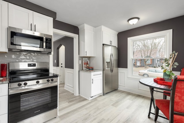 kitchen with white cabinets, light wood-style floors, appliances with stainless steel finishes, and arched walkways