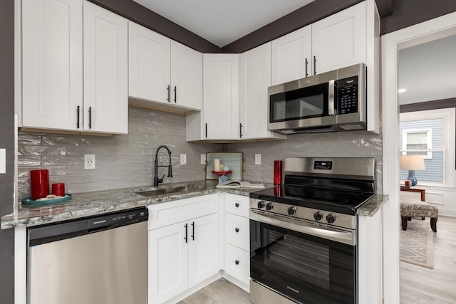 kitchen featuring appliances with stainless steel finishes, a sink, light stone counters, and white cabinets