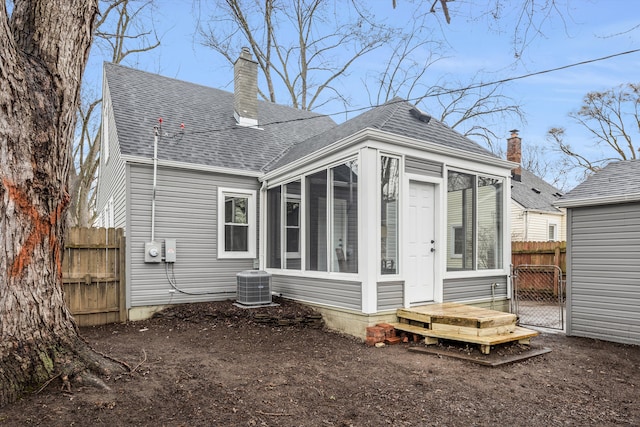 rear view of property with central AC unit, a sunroom, a chimney, roof with shingles, and fence