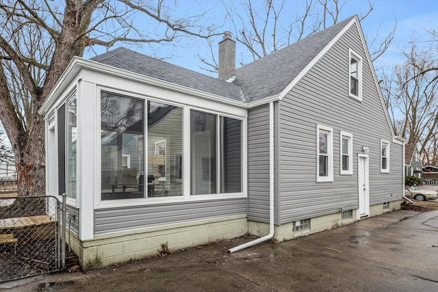 view of property exterior with a sunroom, a shingled roof, a chimney, and fence