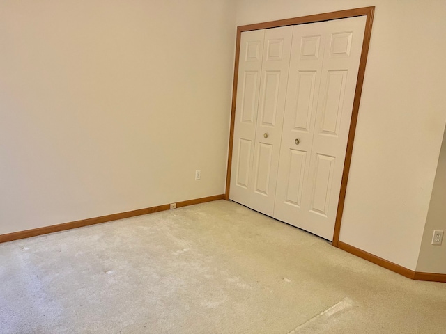 unfurnished bedroom with light carpet, baseboards, and a closet