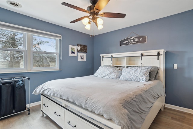 bedroom with a ceiling fan, wood finished floors, visible vents, and baseboards