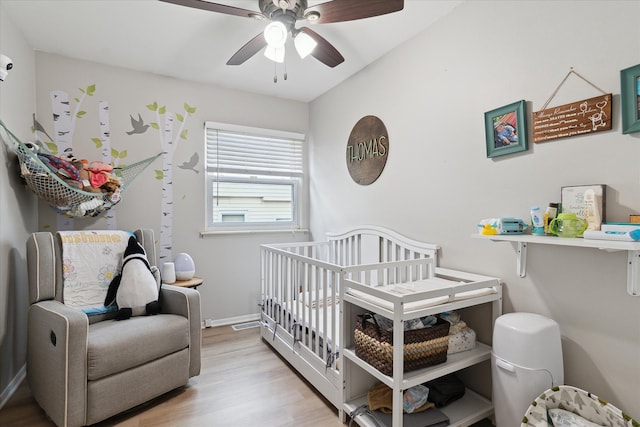 bedroom featuring ceiling fan, a crib, baseboards, and wood finished floors