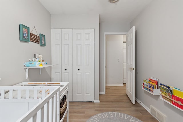 bedroom featuring a crib, baseboards, visible vents, light wood-type flooring, and a closet