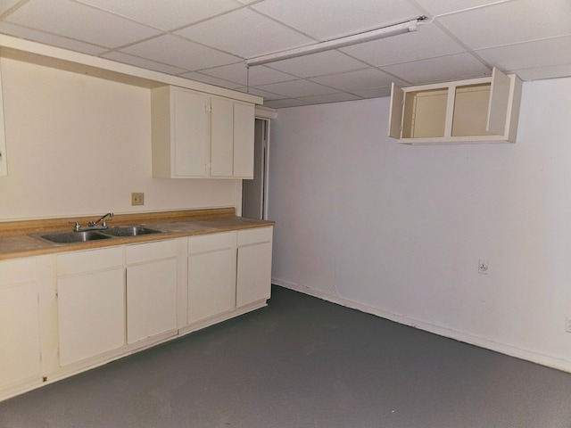 kitchen featuring finished concrete flooring, a sink, a paneled ceiling, and white cabinets