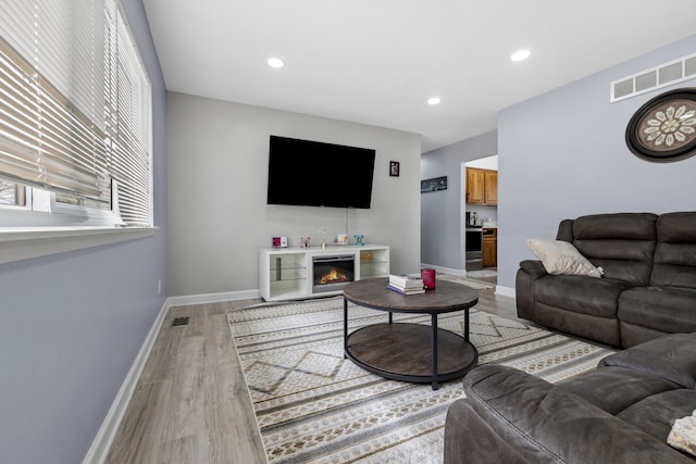 living room featuring a glass covered fireplace, light wood-style flooring, baseboards, and recessed lighting