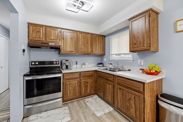 kitchen with electric stove, light countertops, brown cabinetry, a sink, and under cabinet range hood