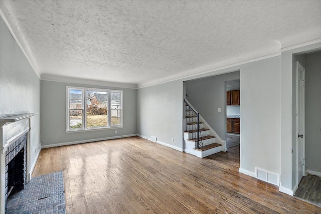 unfurnished living room featuring visible vents, a fireplace with flush hearth, hardwood / wood-style floors, stairs, and crown molding