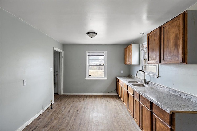 kitchen featuring light countertops, a sink, light wood-style flooring, and baseboards