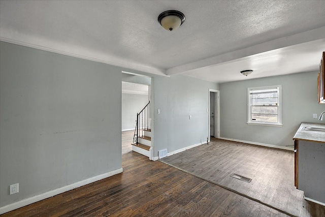 unfurnished room with dark wood-type flooring, a sink, visible vents, baseboards, and stairs