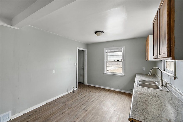 kitchen with baseboards, light wood-style flooring, visible vents, and a sink