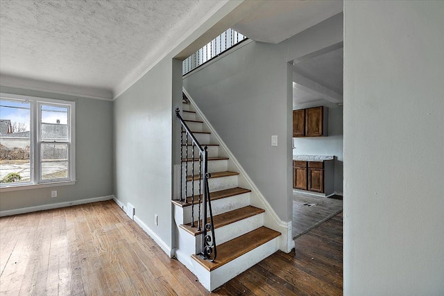 stairway featuring a textured ceiling, baseboards, and hardwood / wood-style floors