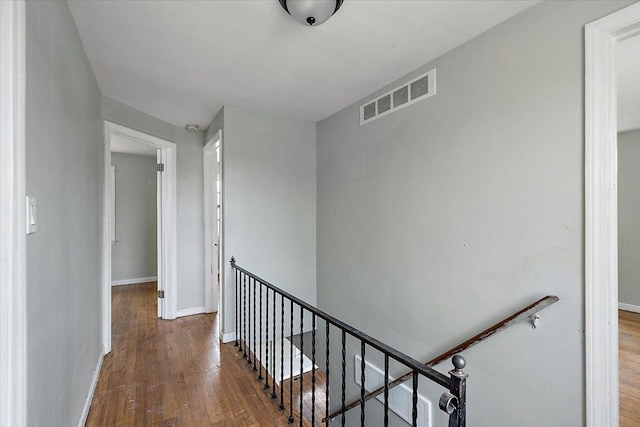 corridor featuring wood-type flooring, visible vents, baseboards, and an upstairs landing