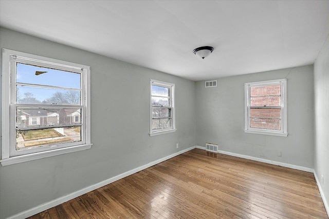 spare room with hardwood / wood-style flooring, visible vents, and baseboards