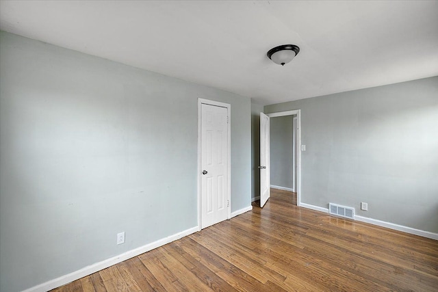 empty room featuring wood finished floors, visible vents, and baseboards