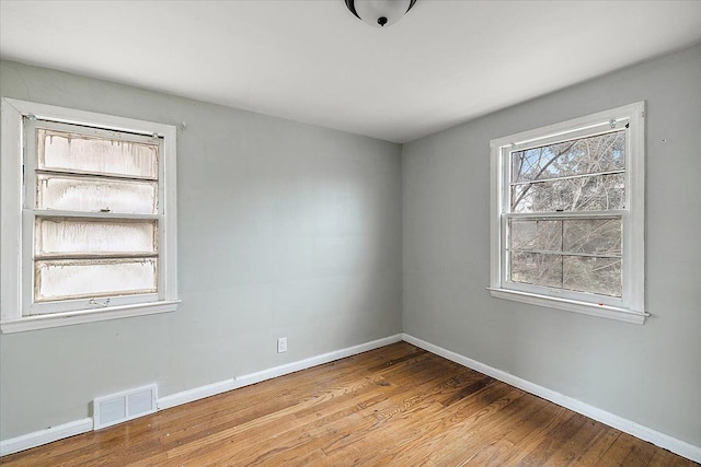 unfurnished room featuring baseboards, visible vents, and wood finished floors