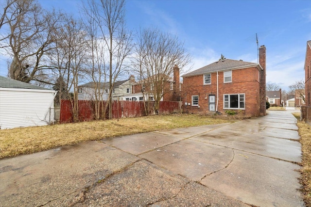 view of home's exterior featuring brick siding, fence, a chimney, and a lawn