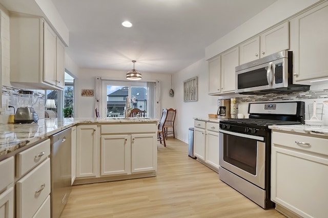 kitchen with light stone counters, light wood-style flooring, stainless steel appliances, a peninsula, and backsplash